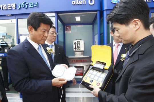지난 2011년 당시 조준희(왼쪽) 기업은행장이 서울역 광장의 길거리 점포에 설치돼 있는 자동심장 충격장치를 살펴보고 있다. (사진=기업은행)