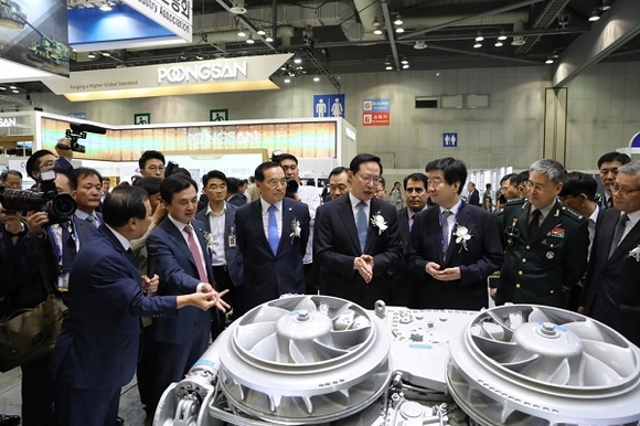 S&T중공업 권정원 사장이 S&T중공업 부스 내 K2 전차 변속기 전시품 앞에서 송영무 국방부 장관(왼쪽 4번째)과 최평규 S&T 회장(한국방위산업진흥회장, 오른쪽 3번째) 등 국내 군 관계자들에게 제품의 기능을 설명하고 있다. (사진=S&T모티브)